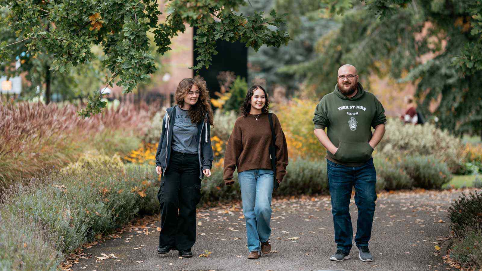 Three students walking together under autumn trees on campus. 
