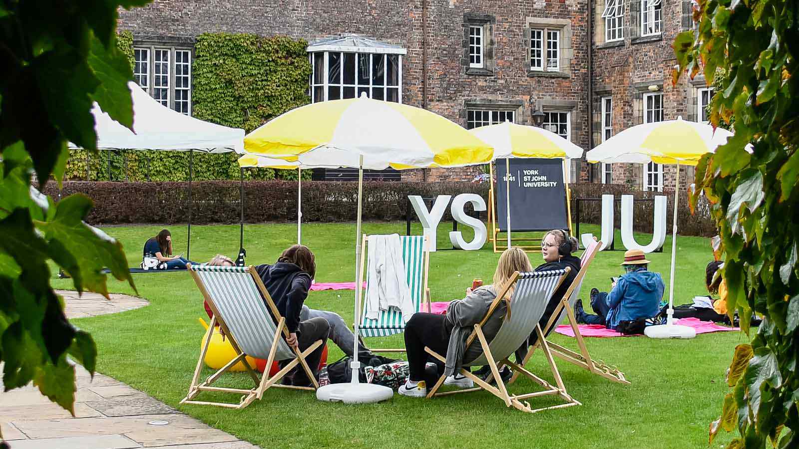 Students sitting in deckchairs at Welcome Week event. Oversized YSJU letters stand in the background. 