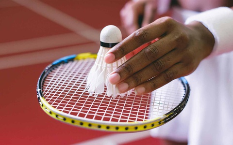 Close up of a hand placing a badminton shuttlecock on a racquet. Photo by SHVETS production on Pexels. 