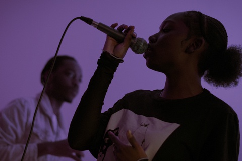 Individual singing into microphone with purple backdrop 