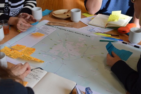 A group of people sat around a table with a map of York on it. 