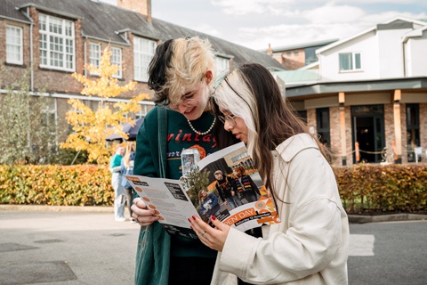 Two prospective students looking at a brochure on an open day. 
