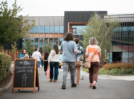 Parents and carers walking with students towards the Creative Centre. A sign is pointing to the Parents and Carers Hub. 