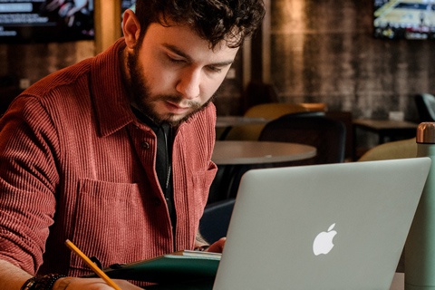 Student sitting at table, writing notes at laptop 