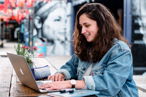 Student typing on laptop at table with notepad and highlighters 