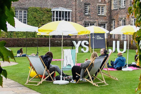 Students sitting together on deck chairs in the Quad at York St John University York Campus 