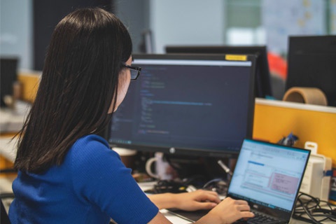 A woman uses a laptop and computer monitor. 