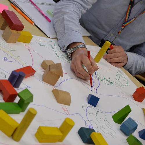 A staff member drawing on a piece of paper that has wooden blocks on top of it. 